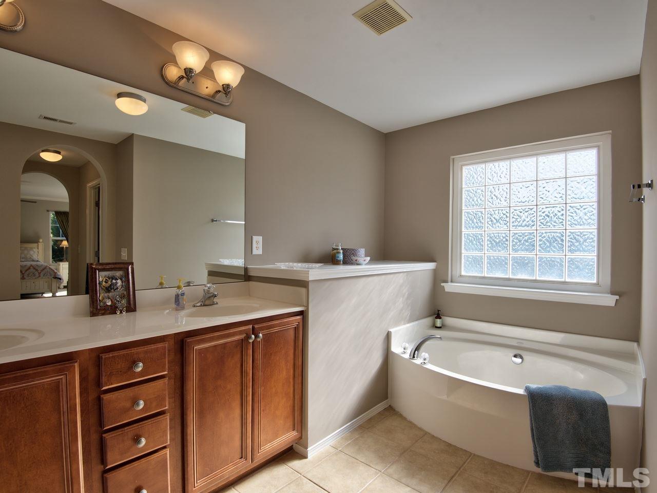 8415 Stonework Drive Raleigh, NC 27613 - Photo 20 of 24 a bathroom with a granite countertop tub a double vanity sink a vanity a window and a mirror
