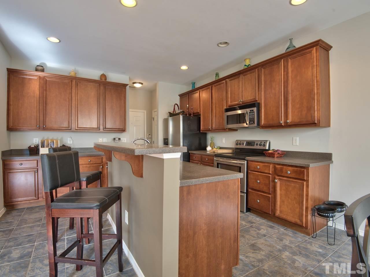 8415 Stonework Drive Raleigh, NC 27613 - Photo 10 of 24 a kitchen with stainless steel appliances granite countertop a stove top oven a sink dishwasher a dining table and chairs with wooden cabinets