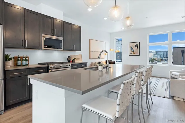 a kitchen with stainless steel appliances granite countertop a sink a stove a refrigerator cabinets and a dining table with wooden floor