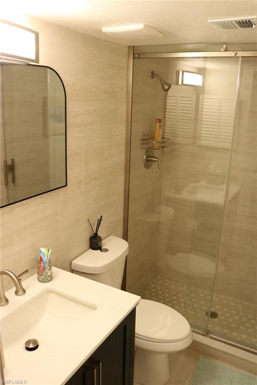 2235 San Marco Road, Unit 5204 Marco Island, FL 34145 - Photo 19 of 34 Bathroom featuring a walk-in shower with a glass enclosure, tiled walls, and a pebble-style floor