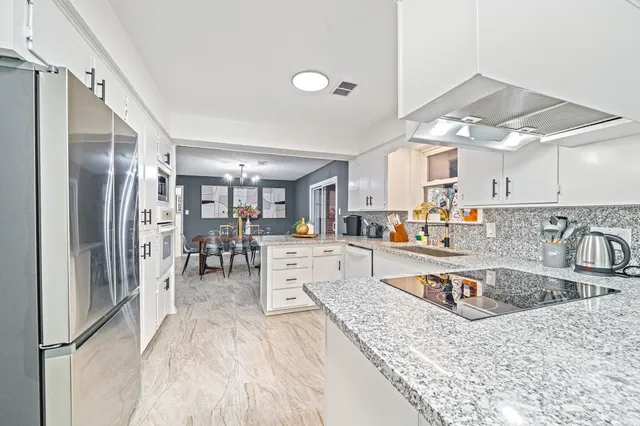 a kitchen with stainless steel appliances granite countertop a refrigerator a sink dishwasher a stove with white cabinets and wooden floor