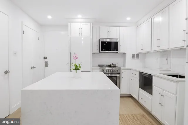 a kitchen with stainless steel appliances a stove top oven a sink a refrigerator and white cabinets