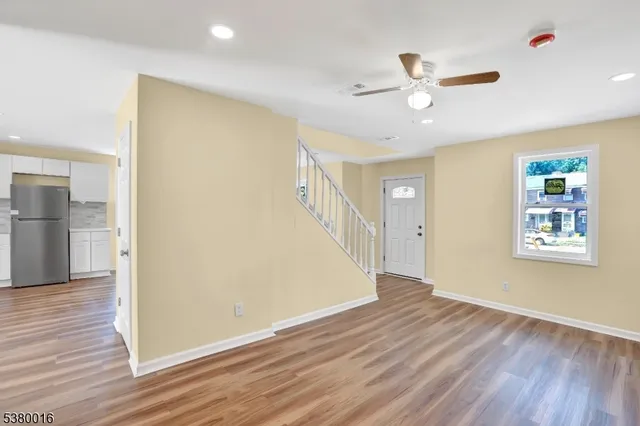a view of an empty room with wooden floor and a ceiling fan