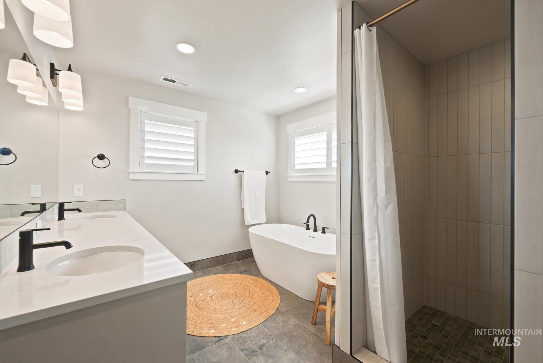 6933 South Zenith Avenue Meridian, ID 83642 - Photo 28 of 34 Bathroom featuring a double vanity with undermount sinks and matte black fixtures, a freestanding soaking tub, and a glass-enclosed shower with vertical tile work