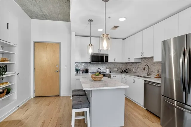 a kitchen with stainless steel appliances granite countertop a refrigerator a sink dishwasher a stove and white cabinets with wooden floor