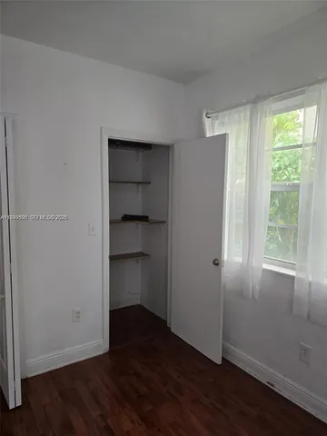 an empty room with wooden floor closet and windows
