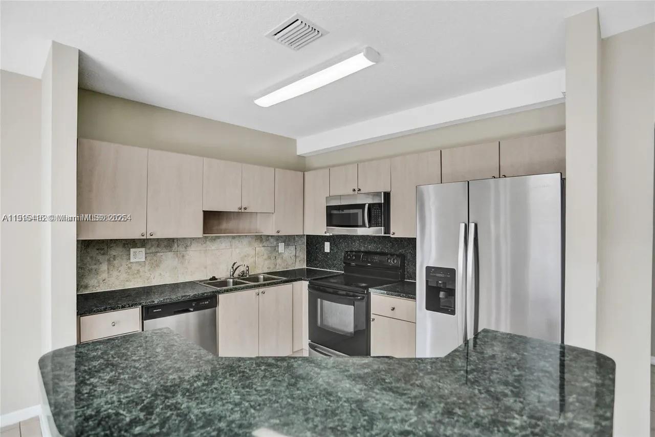 2802 Southwest 128th Way Miramar, FL 33027 - Photo 17 of 37 a kitchen with stainless steel appliances granite countertop a refrigerator a stove a sink a microwave a oven and white cabinets