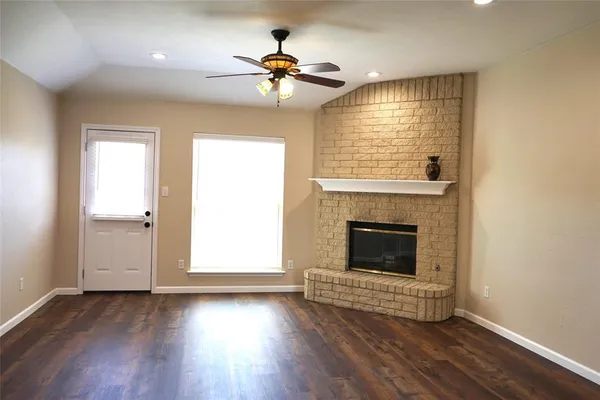 an empty room with wooden floor fireplace and windows