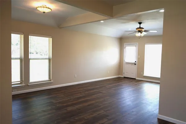 an empty room with wooden floor ceiling fan and windows