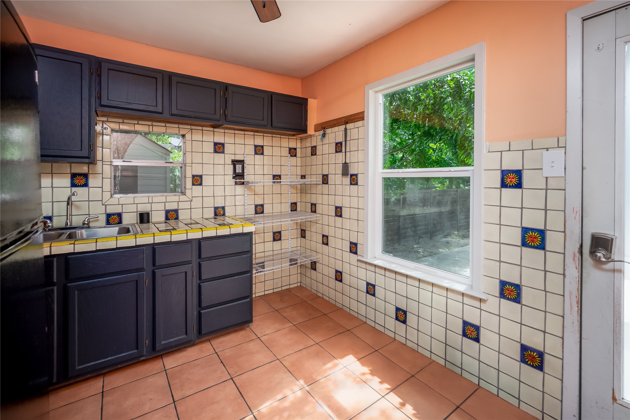 719 Springdale Road Austin, TX 78702 - Photo 14 of 17 A quaint kitchen boasts vibrant tiled walls, deep-toned cabinetry, and a sun-drenched window overlooking lush private backyard .