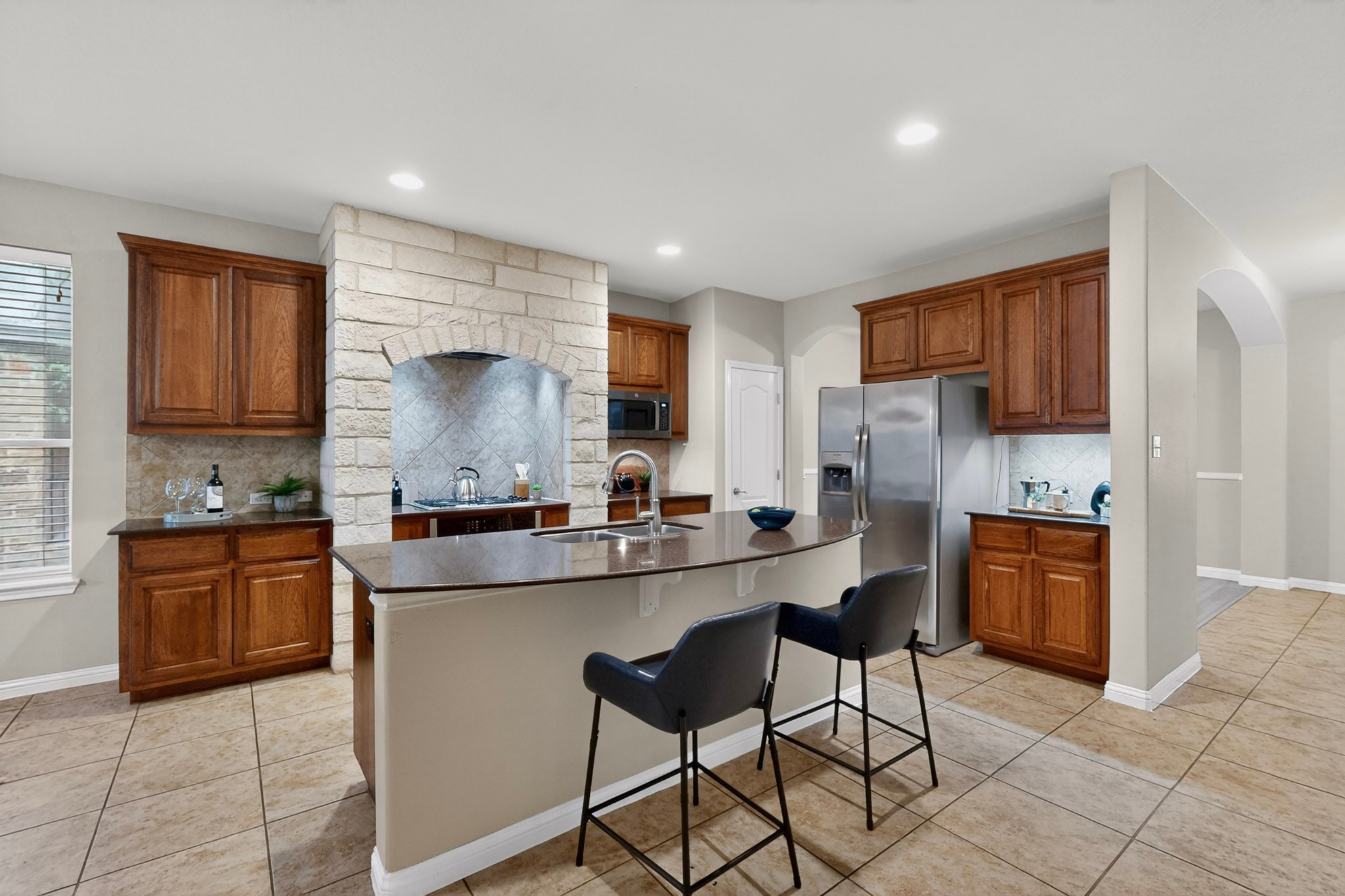 178 Limestone Trail Austin, TX 78737 - Photo 16 of 40 Spacious kitchen featuring a stone archway, wood cabinetry, tile flooring, an island with countertop seating, and stainless steel appliances