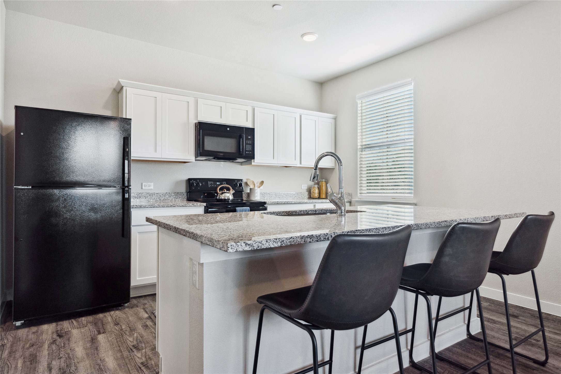 523 Powell Drive, Unit 1101 Leander, TX 78641 - Photo 7 of 24 Kitchen featuring black appliances, white cabinets, a kitchen bar, and dark wood-style flooring