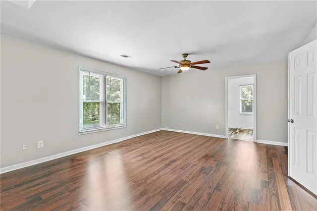 an empty room with wooden floor chandelier fan and windows