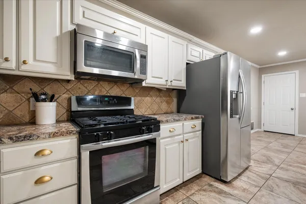 a kitchen with stainless steel appliances granite countertop white cabinets a stove a microwave and a refrigerator