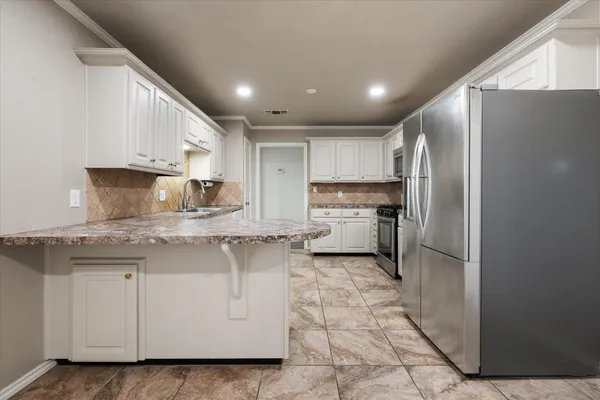 a kitchen with kitchen island granite countertop a refrigerator a sink and white cabinets