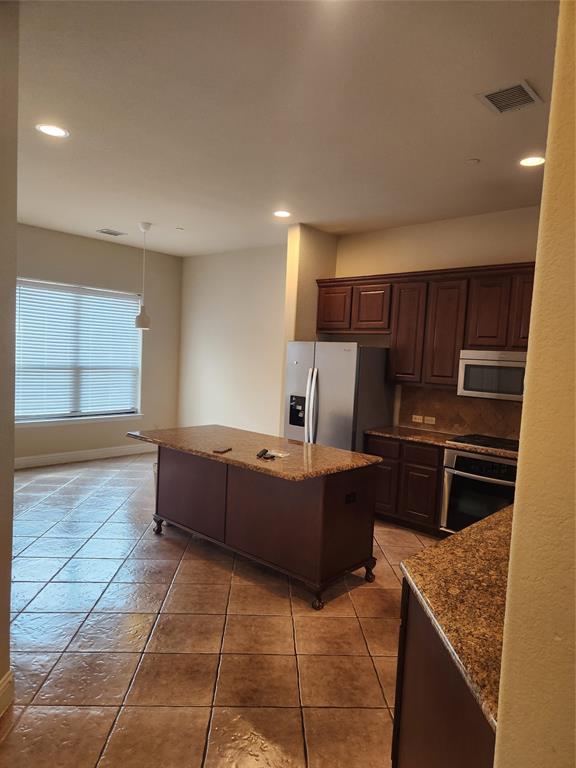 5720 Robbie Road Plano, TX 75024 - Photo 7 of 30 Kitchen featuring an island with stone-finish countertop, stainless steel appliances, dark wood-finish cabinetry, tile flooring, and recessed lighting