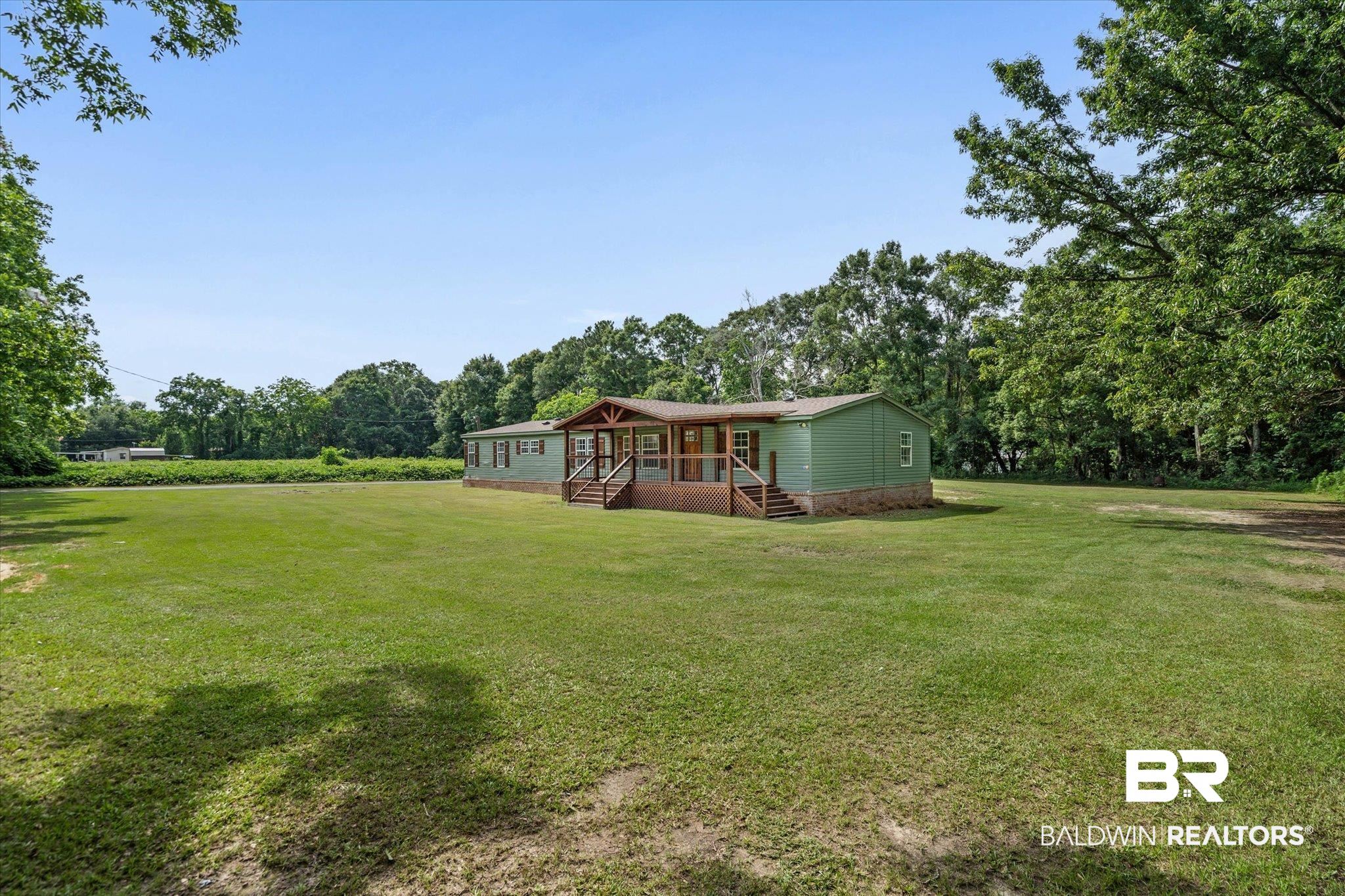 9230 McLeod Road Mobile, AL 36695 - Photo 2 of 20 Expansive green lawn surrounds this property featuring a covered front porch with wood railings and steps, light green siding, and a partial stone facade