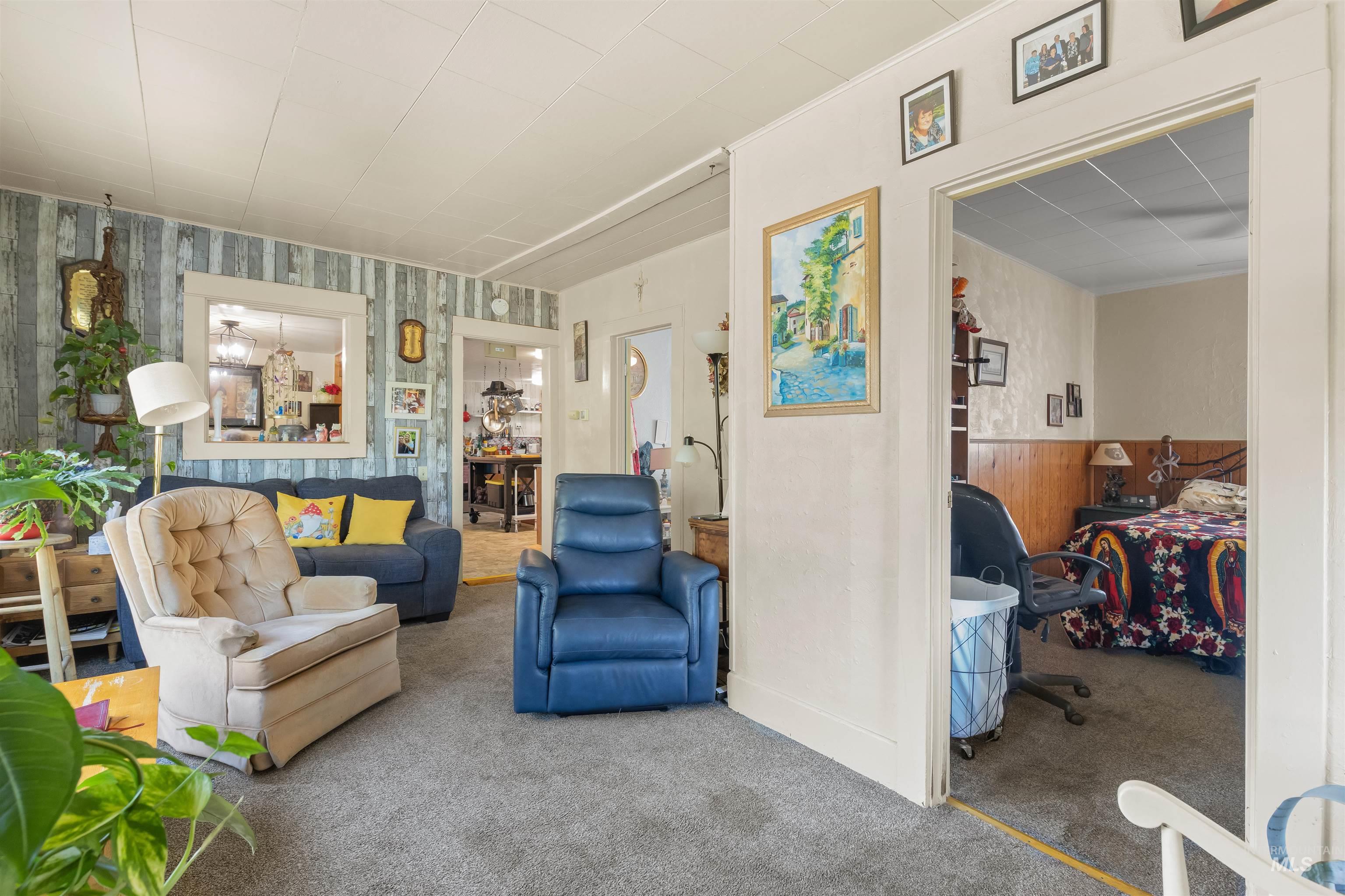 238 Hillcrest Road Lewiston, ID 83501 - Photo 23 of 27 Carpeted living area featuring a large pass-through window with trim, light-toned ceiling panels, and a doorway to an additional room with wood paneling