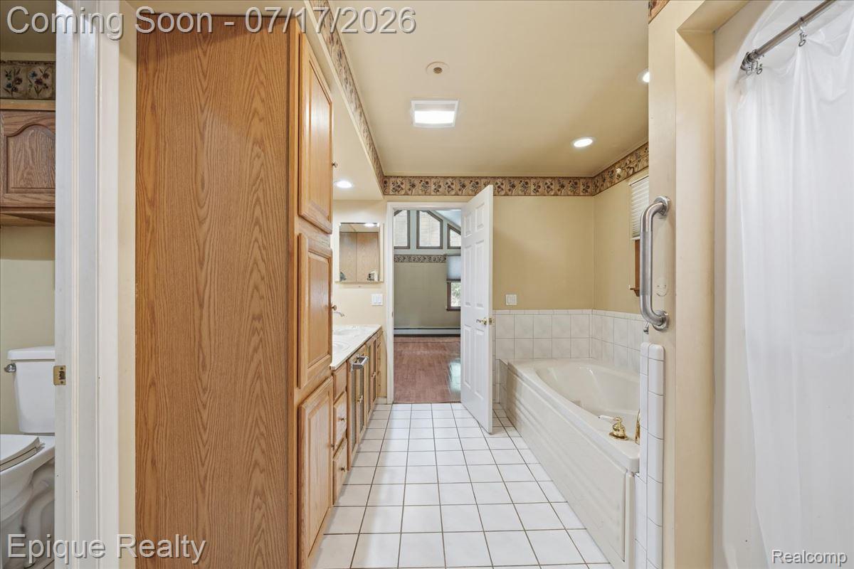 22520 Waltz Road New Boston, MI 48164 - Photo 30 of 43 Bathroom featuring white square tile flooring, a built-in bathtub with tiled surround, a vanity with light-toned wood-finish cabinetry and a light-toned countertop, and a shower with a grab bar