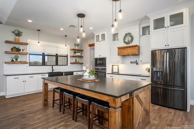 a kitchen with stainless steel appliances granite countertop a stove a refrigerator a oven a sink a dining table and chairs with wooden floor