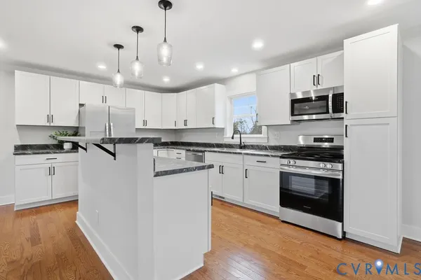 a kitchen with granite countertop a refrigerator a sink and white cabinets