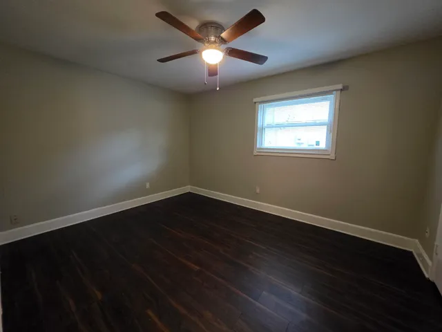 a view of an empty room with wooden floor and a ceiling fan
