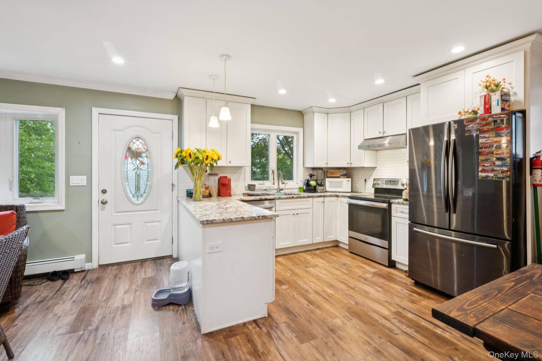 39 Willow Road Rocky Point, NY 11778 - Photo 9 of 18 Kitchen featuring stainless steel appliances, a peninsula, light wood-style floors, tasteful backsplash, and hanging light fixtures