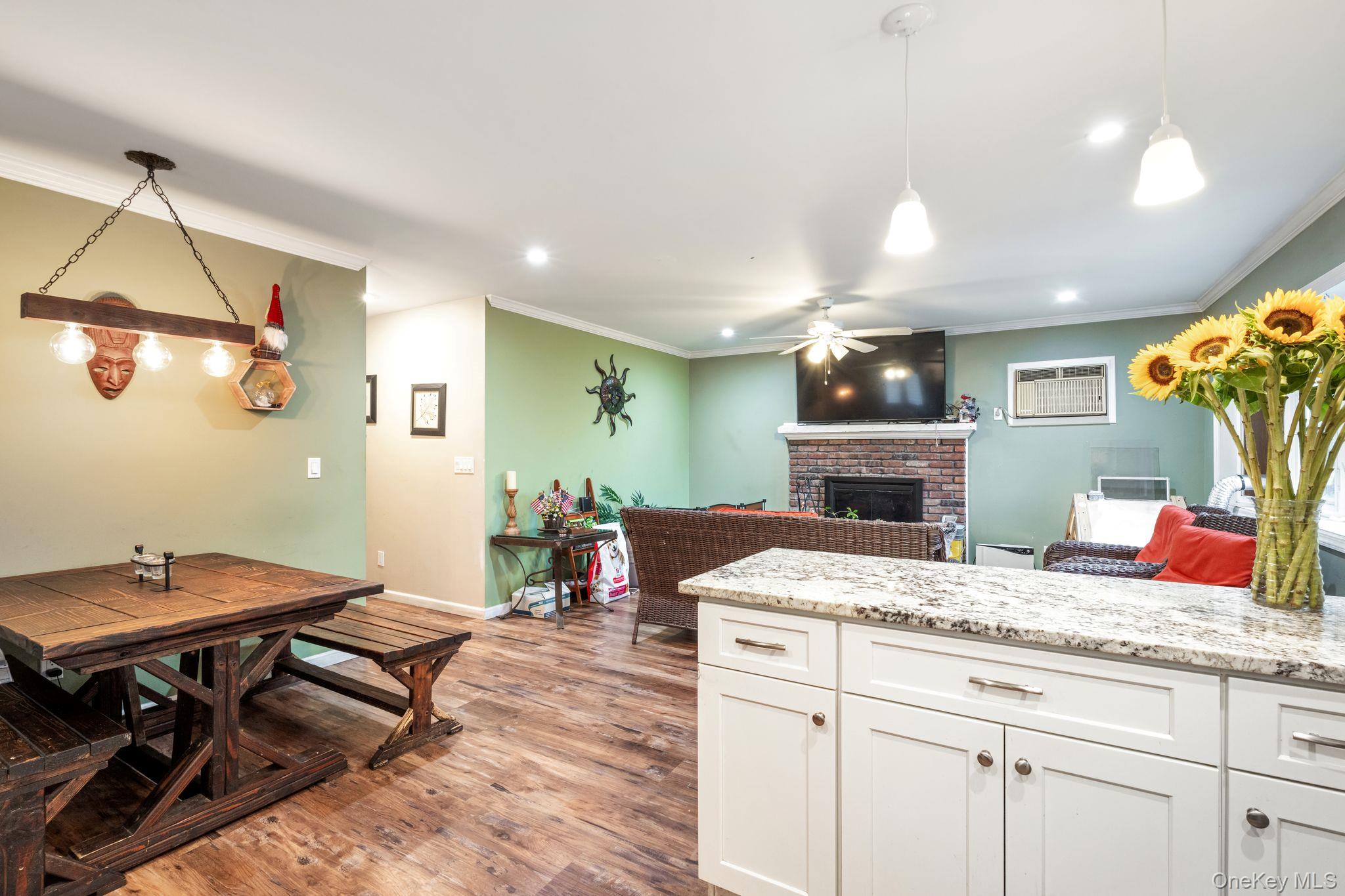 39 Willow Road Rocky Point, NY 11778 - Photo 16 of 18 Kitchen featuring light wood-style floors, a brick fireplace, crown molding, white cabinetry, and open floor plan