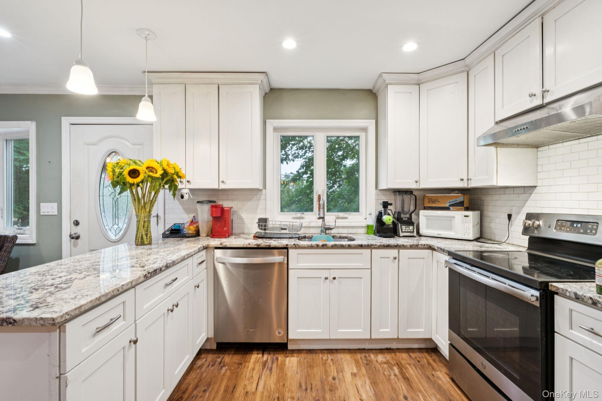 39 Willow Road Rocky Point, NY 11778 - Photo 8 of 18 Kitchen featuring stainless steel appliances, light wood-style floors, a peninsula, under cabinet range hood, and white cabinetry