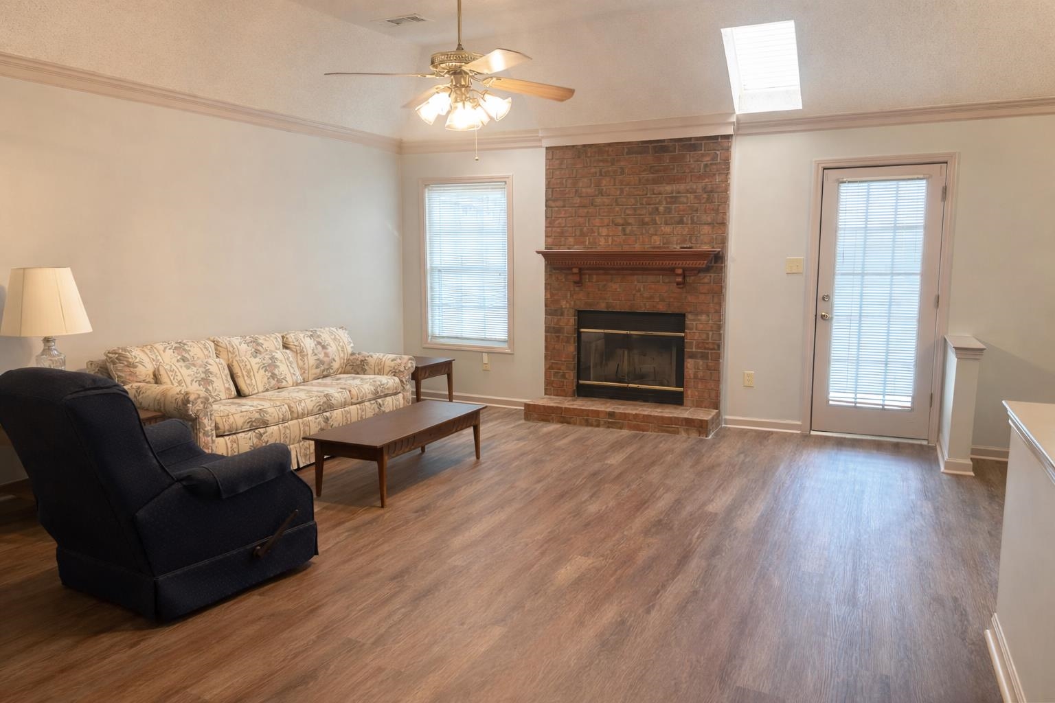 6708 Dawnhill Road Bartlett, TN 38135 - Photo 3 of 18 Spacious living area featuring wood-finish flooring, a brick fireplace with a wood mantel, a ceiling fan with integrated lighting, a skylight, and a glass-paneled exterior door