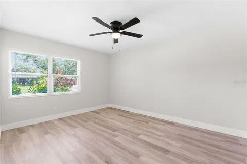 an empty room with wooden floor ceiling fan and windows