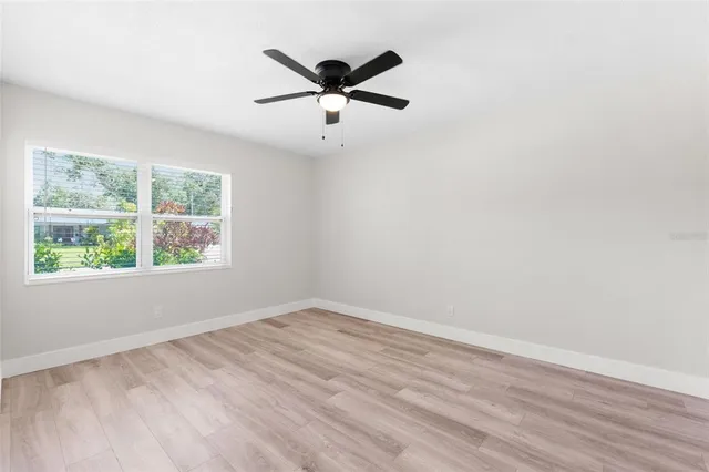 an empty room with wooden floor ceiling fan and windows