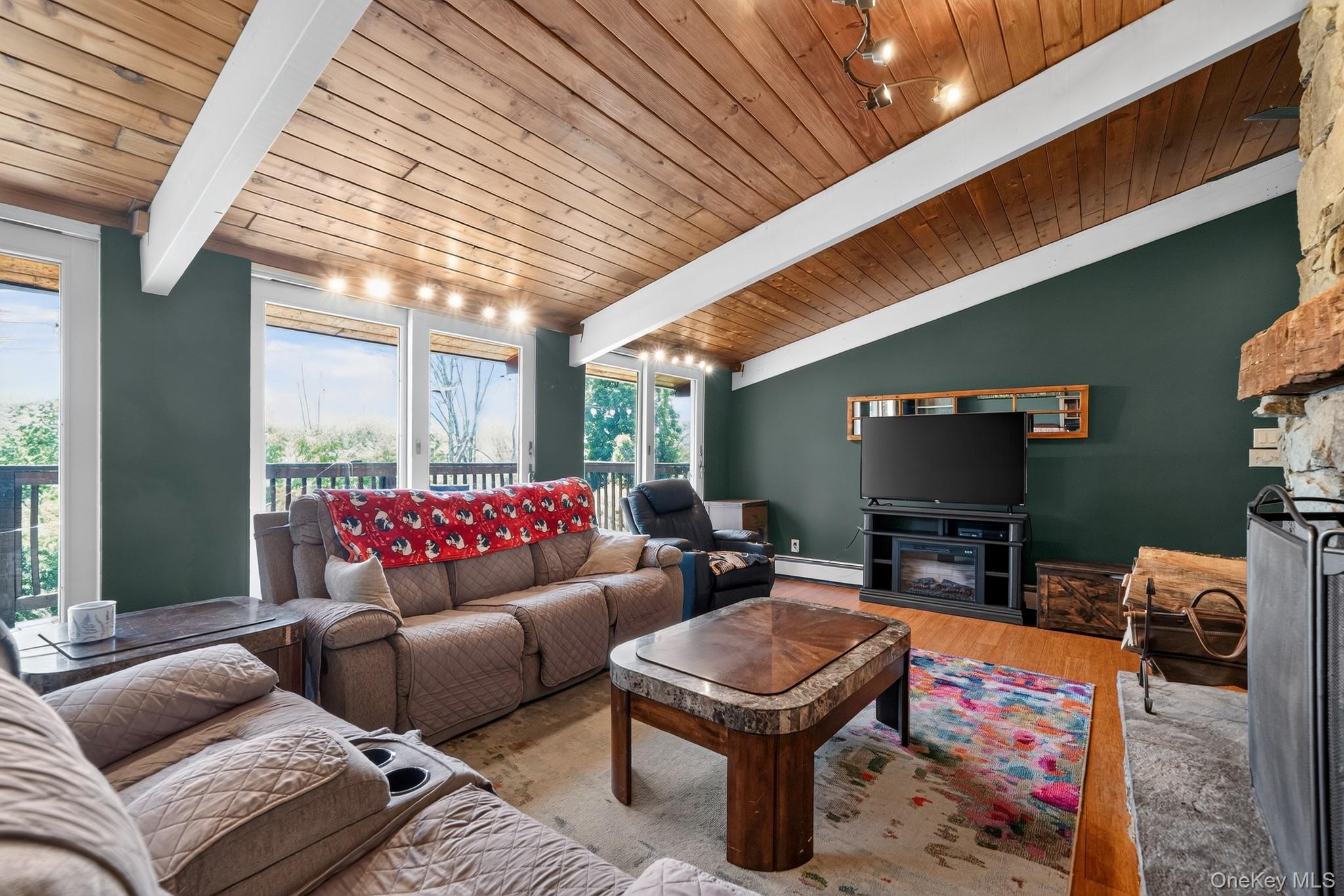 424 Laroe Road Chester, NY 10918 - Photo 36 of 43 Living area featuring an exposed beam wood-paneled ceiling, large windows, a stone-faced fireplace with a natural wood mantel, and wood-finish flooring