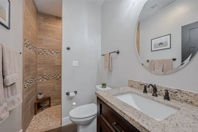 a bathroom with a granite countertop sink a toilet a mirror and shower