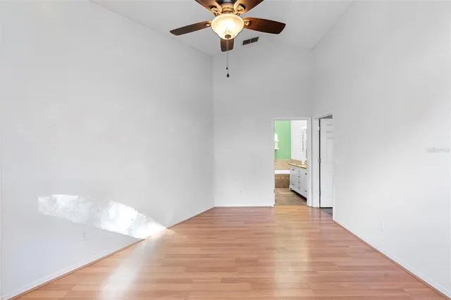 a view of an empty room with wooden floor and a ceiling fan