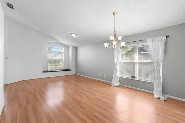 an empty room with wooden floor chandelier and windows