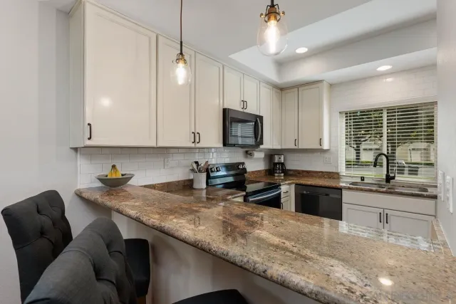 a kitchen with granite countertop a stove a sink a microwave a dining table and chairs