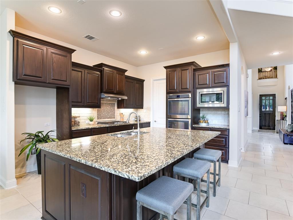 2657 Montebelluna Place Leander, TX 78641 - Photo 7 of 29 Kitchen featuring dark brown cabinetry, tasteful backsplash, a breakfast bar area, light stone countertops, and recessed lighting