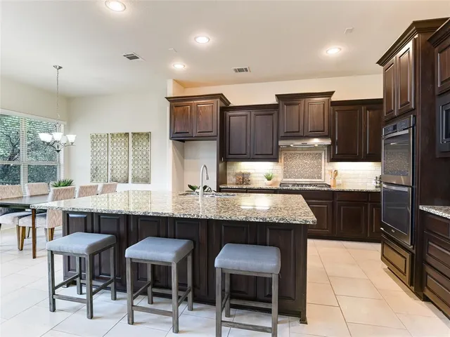 a kitchen with stainless steel appliances kitchen island granite countertop a table chairs sink and cabinets