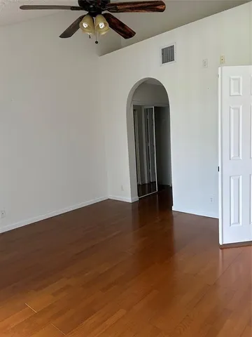 a view of an empty room with wooden floor and a ceiling fan