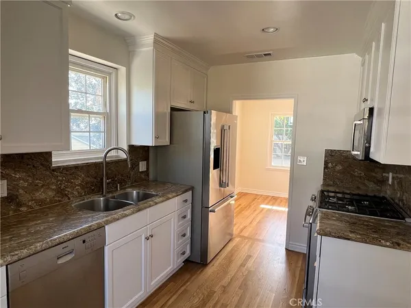 a kitchen with granite countertop a refrigerator a sink a stove and wooden floor