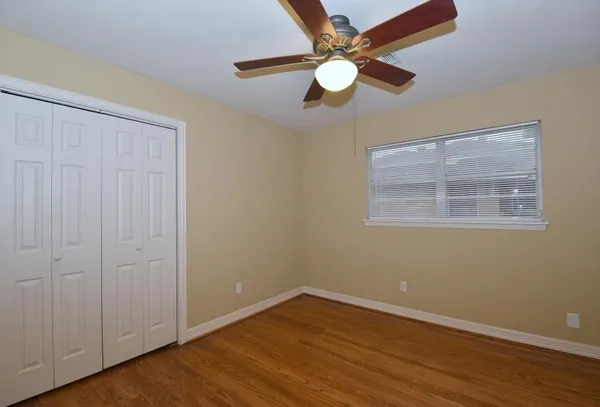 an empty room with wooden floor fan and windows