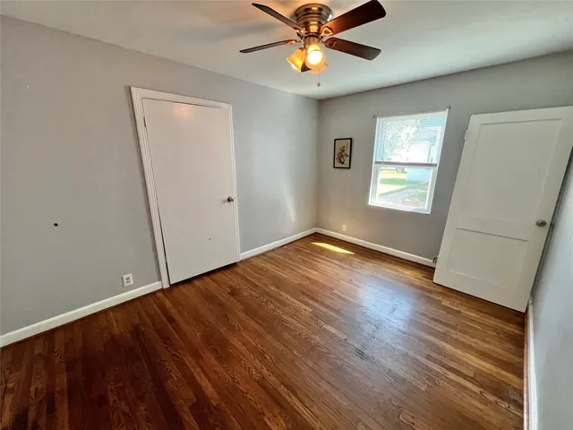 an empty room with wooden floor fan and windows