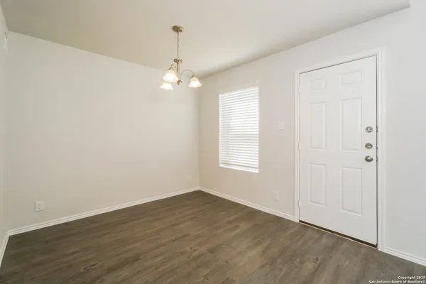 an empty room with wooden floor chandelier fan and windows