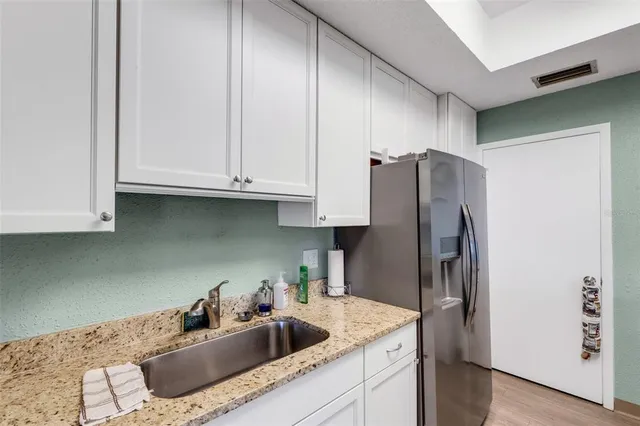 a kitchen with stainless steel appliances granite countertop a refrigerator a sink and white cabinets