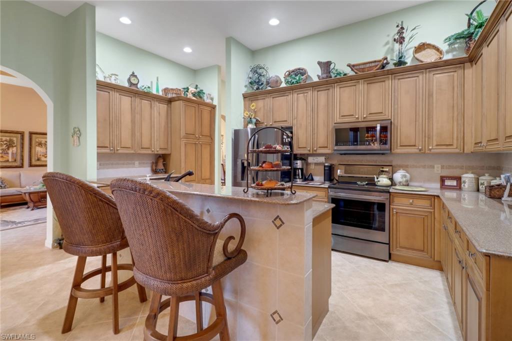 20531 Foxworth Circle Estero, FL 33928 - Photo 8 of 50 Kitchen with a kitchen bar, light stone countertops, a center island, light tile patterned flooring, and stainless steel appliances