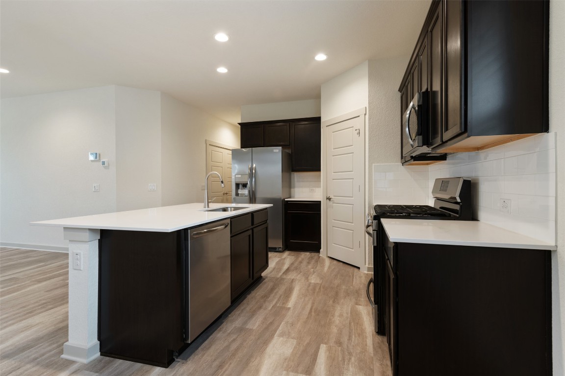 220 Deserti Road Leander, TX 78641 - Photo 7 of 16 Kitchen with appliances with stainless steel finishes, an island with sink, light wood-style floors, backsplash, and light countertops