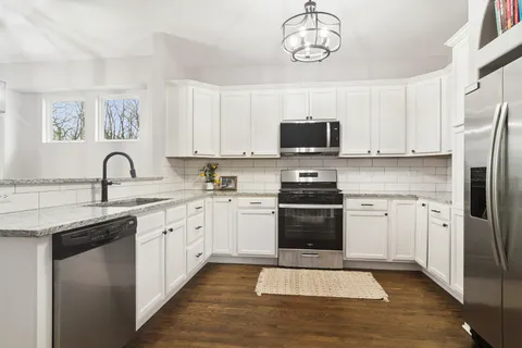 a kitchen with stainless steel appliances granite countertop a stove top oven a sink dishwasher and a refrigerator with wooden cabinets