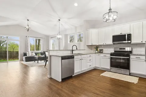 a kitchen with stainless steel appliances a stove a sink dishwasher a refrigerator and a dining table with wooden floor