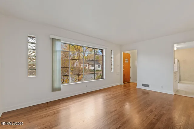 a view of an empty room with wooden floor and a window